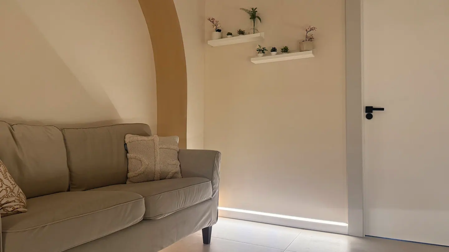 The lounge: a linen sofa against an ochre arch, lit along the skirting.